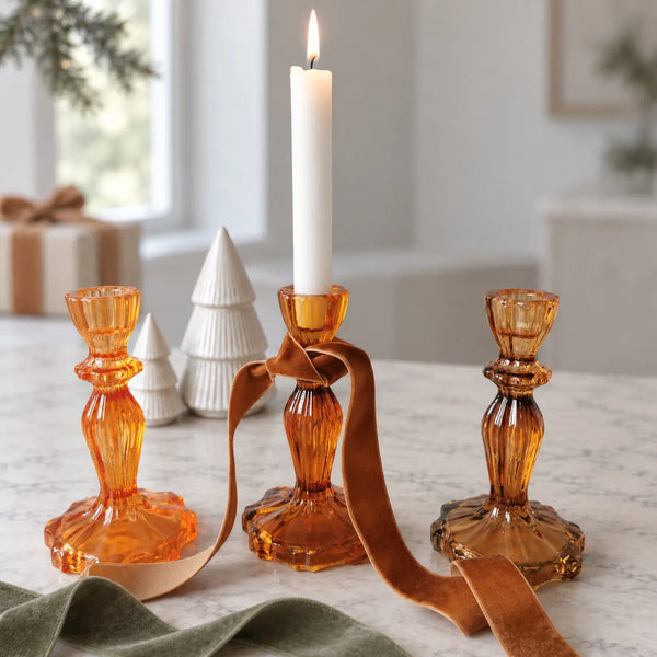 Three ribbed candlestick holders in orange and amber tones, with a ribbon tied around the centre holder.