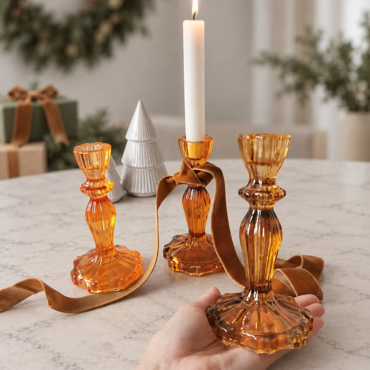 Cognac-toned candlestick holder held in one hand, showing its ribbed stem and scalloped base.