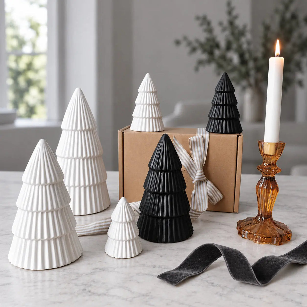 Four white and two black ribbed ceramic Christmas trees beside a gift box and amber candleholder by Almasea