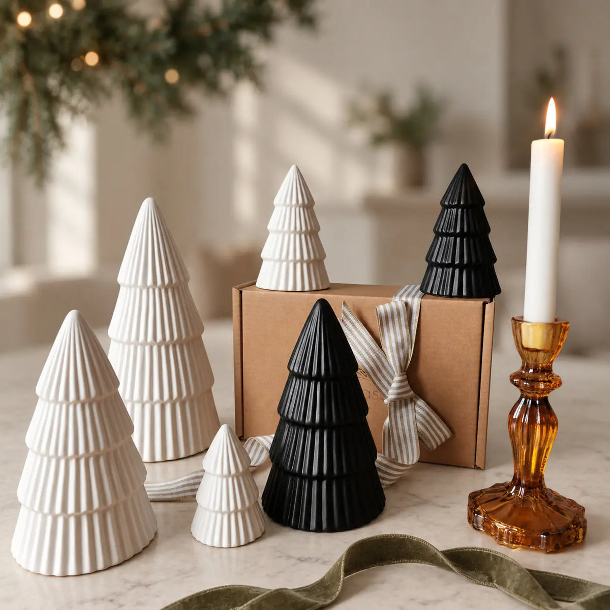 Four white and two black ribbed ceramic Christmas trees beside a gift box and amber candleholder by Almasea