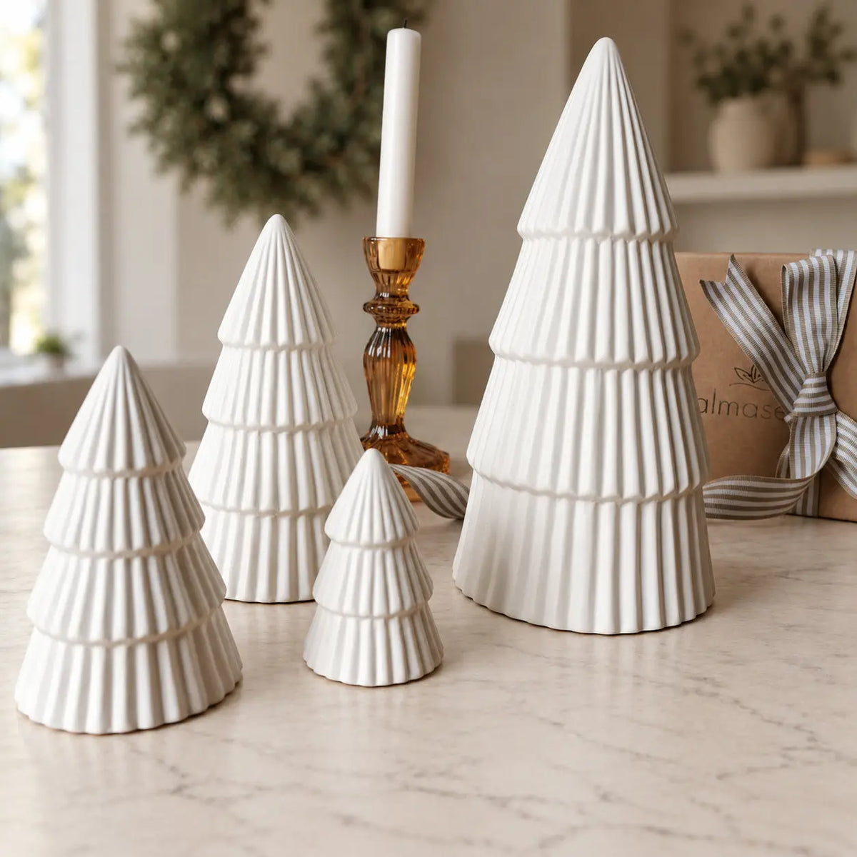 Four ribbed ceramic Christmas trees beside a gift box and amber candleholder by Almasea