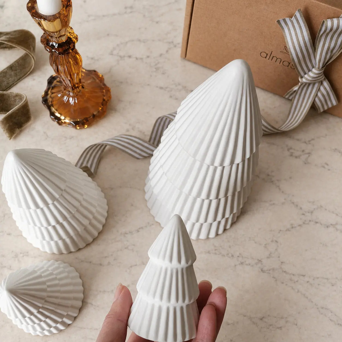 Four ribbed ceramic Christmas trees beside a gift box and amber candleholder by Almasea