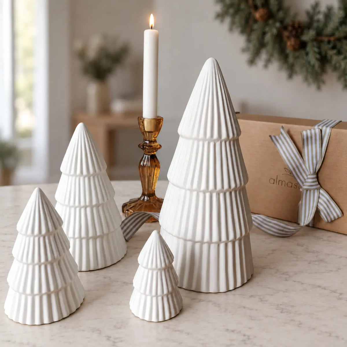 Four ribbed ceramic Christmas trees beside a gift box and amber candleholder by Almasea