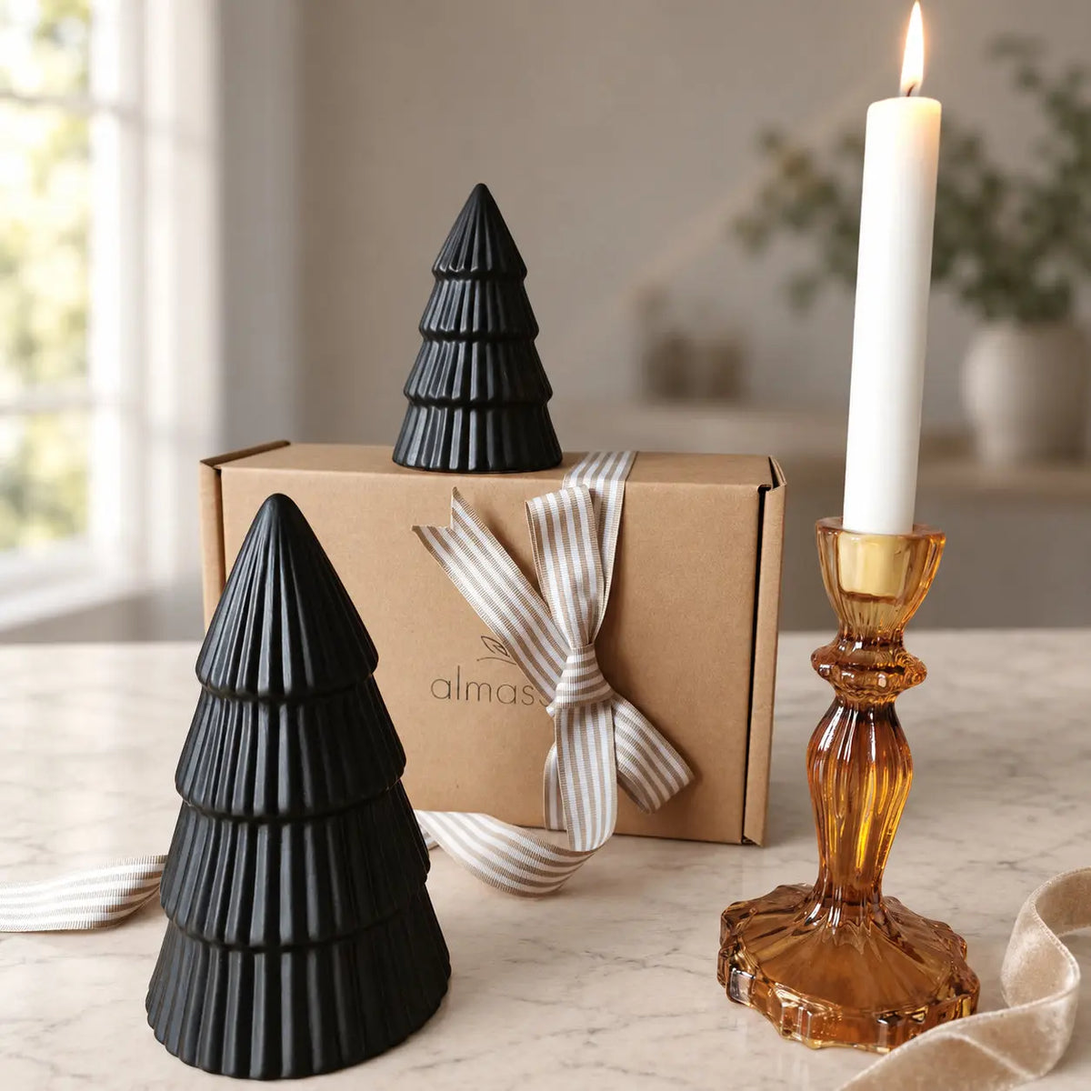 Two black ribbed ceramic Christmas trees beside a gift box and amber candleholder by Almasea