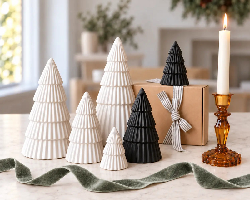 Four white and two black ribbed ceramic Christmas trees beside a gift box and amber candleholder by Almasea